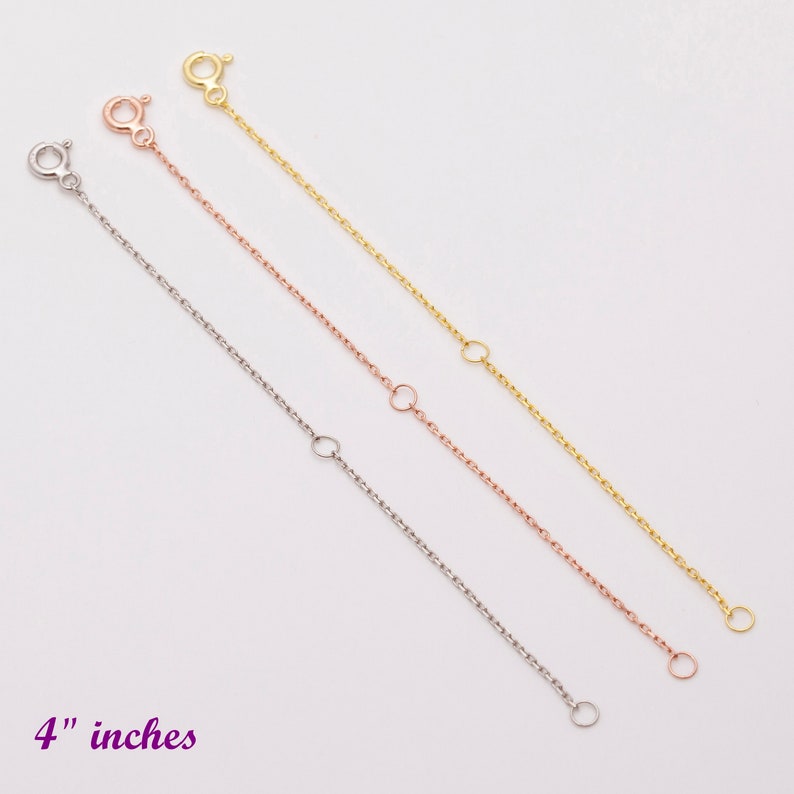 May include: Three gold chain extenders in different colors: yellow gold, rose gold, and white gold. Each extender is 4 inches long and has a lobster clasp on one end and a jump ring on the other end.