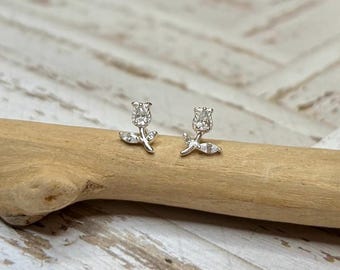 May include: A pair of silver stud earrings with a small flower design. Each earring features a single clear stone in the center of the flower, surrounded by smaller clear stones.
