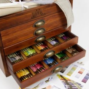 May include: A wooden drawer organiser with five drawers, each filled with spools of colourful embroidery floss. The drawers have brass handles and the top drawer has an engraved design.