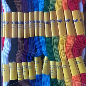 May include: A rainbow assortment of embroidery floss in a clear plastic container. The floss is arranged by color, with shades of red, orange, yellow, green, blue, and purple. Each skein is labeled with text that includes "China" and "8 m".
