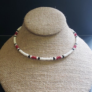 May include: A white beaded necklace with red and black beads.