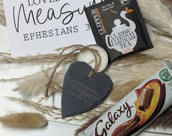 May include: A gift basket with a black slate heart that says "Loved Beyond Measure Ephesians 3:19", a tea bag, a chocolate bar, and a small white candle.