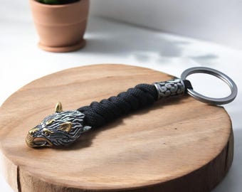 May include: A black paracord keychain with a silver wolf head charm and a silver ring. The wolf head has gold accents.