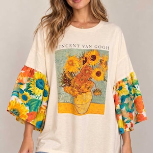 May include: An off-white t-shirt featuring a graphic print of Vincent van Gogh's Sunflowers painting on the chest. The shirt has voluminous, elbow-length sleeves with a vibrant, multicolored sunflower and floral pattern.
