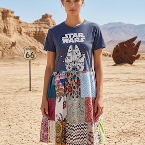 May include: A navy blue t-shirt dress featuring the Star Wars logo and a graphic of the Millennium Falcon. The dress has a patchwork skirt with various floral and geometric patterns. A Route 66 sign is visible in the background.
