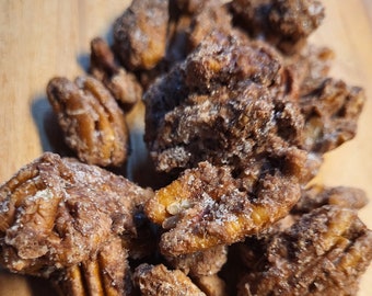 May include: A close-up of a pile of pecan pieces coated in a dark brown chocolate and sprinkled with white sugar crystals.