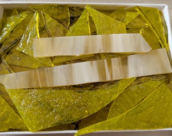 May include: A white box filled with pieces of yellow and off-white glass. The yellow glass pieces are triangular and irregular in shape. Two rectangular pieces of off-white glass are also present.