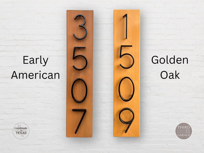 May include: Two wooden house number signs with black numbers. The sign on the left is labeled "Early American" and the sign on the right is labeled "Golden Oak".