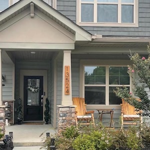 May include: A wooden house with a gray siding and a brown wooden door. The house has a porch with two rocking chairs and a small table. The house number is 13524, which is displayed on a wooden sign.