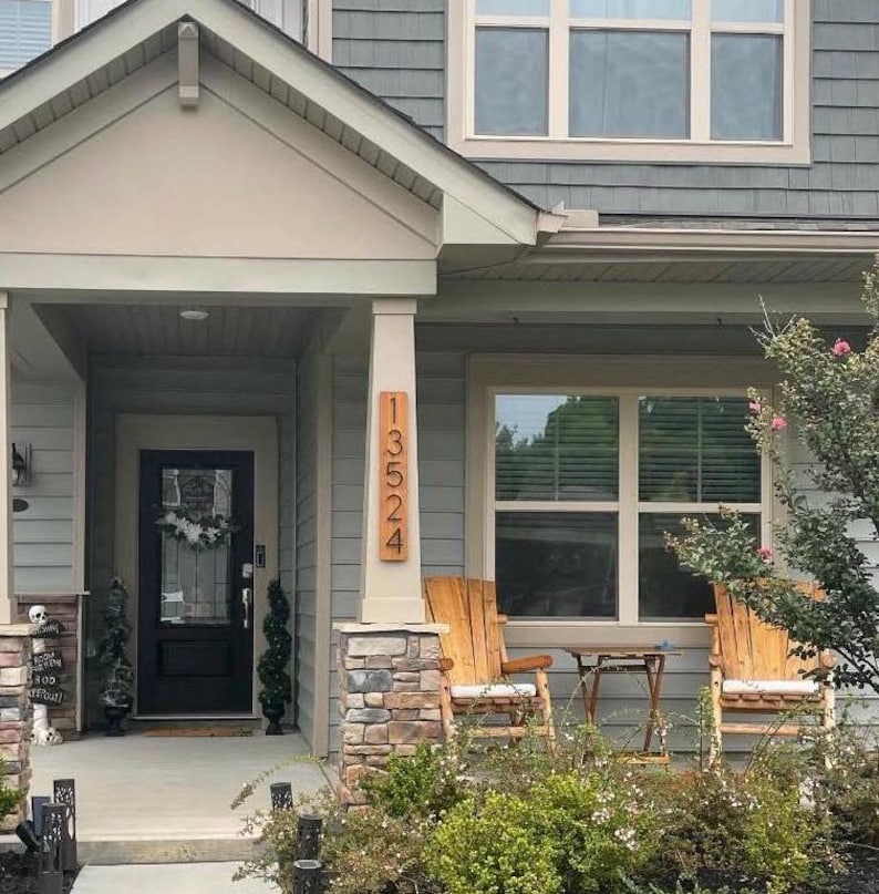 May include: A wooden house with a gray siding and a brown wooden door. The house has a porch with two rocking chairs and a small table. The house number is 13524, which is displayed on a wooden sign.