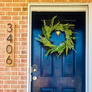 May include: A blue front door with a black metal house number plaque that reads "3406". A green fern wreath hangs on the door. A gold door handle and a digital door lock are visible.