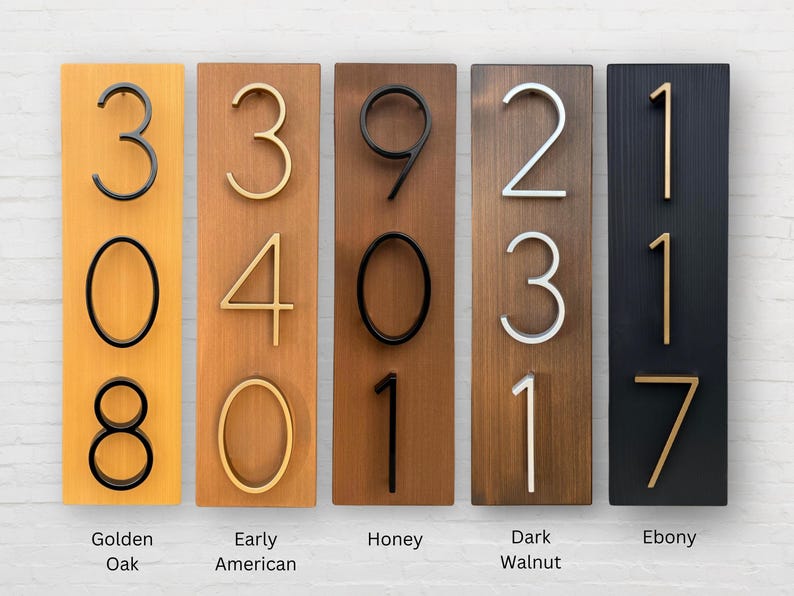 May include: Five wooden signs with different wood stains, each displaying a set of house numbers. The signs are labeled with the wood stain names: Golden Oak, Early American, Honey, Dark Walnut, and Ebony.