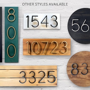 May include: A selection of house number signs in various styles and colours. The numbers are made from metal and are mounted on different types of wood. The numbers include 5930, 800, 1543, 10723, 3325, 564, and 832.