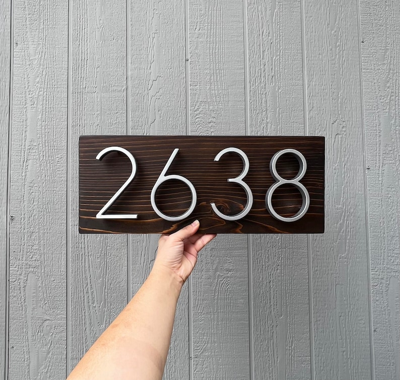 May include: A dark brown wooden sign with the house number 2638 in silver metal lettering.