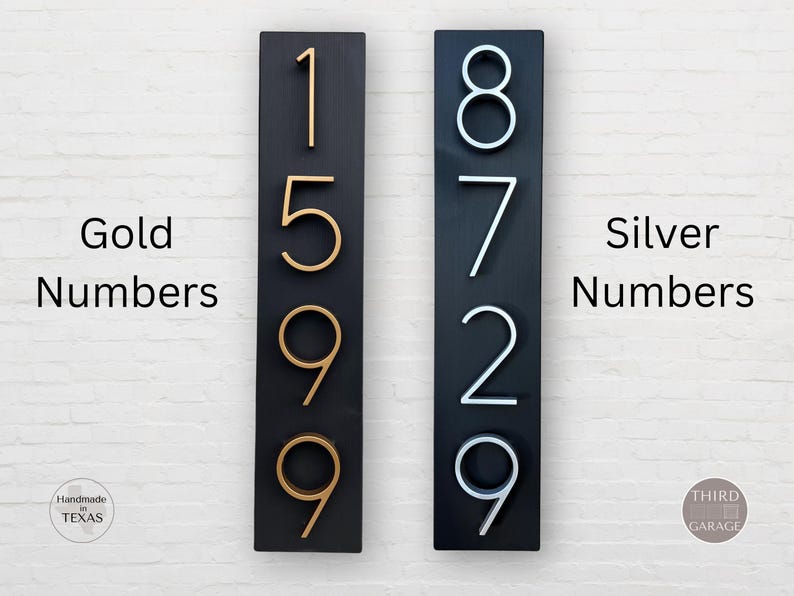 May include: Two black rectangular signs with house numbers. The numbers on the left sign are gold and read 1599. The numbers on the right sign are silver and read 8729. The text "Gold Numbers" is to the left of the left sign and the text "Silver Numbers" is to the right of the right sign.