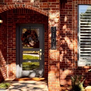 Puede incluir: Una casa de ladrillo con una puerta delantera negra y una placa de n&uacute;mero de casa de metal negro que dice "3101".