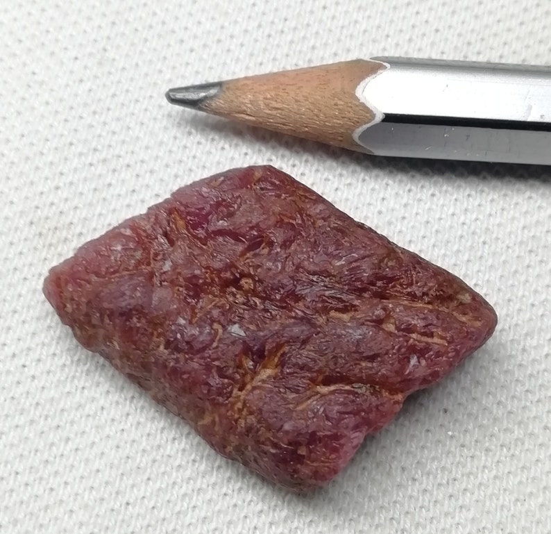Peut inclure: Une pierre pr&eacute;cieuse de rubis rouge fonc&eacute; brute de forme l&eacute;g&egrave;rement rectangulaire. Le rubis est &agrave; peu pr&egrave;s de la taille d'une gomme &agrave; effacer.