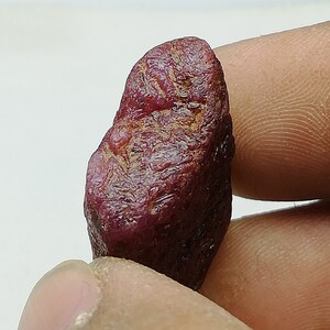 Peut inclure: Une pierre pr&eacute;cieuse de rubis rouge fonc&eacute; avec une surface brute et naturelle. Le rubis est une pierre brute non polie avec une couleur riche et vibrante.