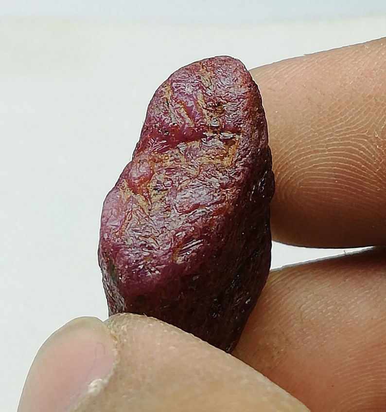 Peut inclure: Une pierre pr&eacute;cieuse de rubis rouge fonc&eacute; avec une surface brute et naturelle. Le rubis est une pierre brute non polie avec une couleur riche et vibrante.