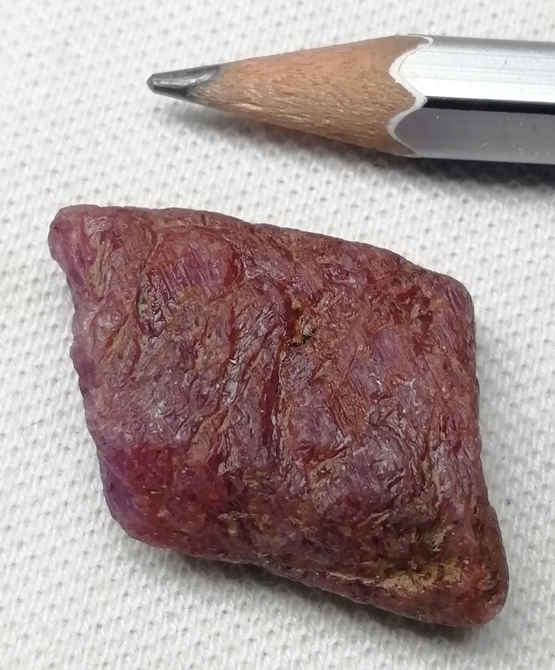 Peut inclure: Une pierre pr&eacute;cieuse de rubis rouge fonc&eacute; brute de forme l&eacute;g&egrave;rement rectangulaire. Le rubis est &agrave; peu pr&egrave;s de la taille d'une gomme &agrave; effacer.
