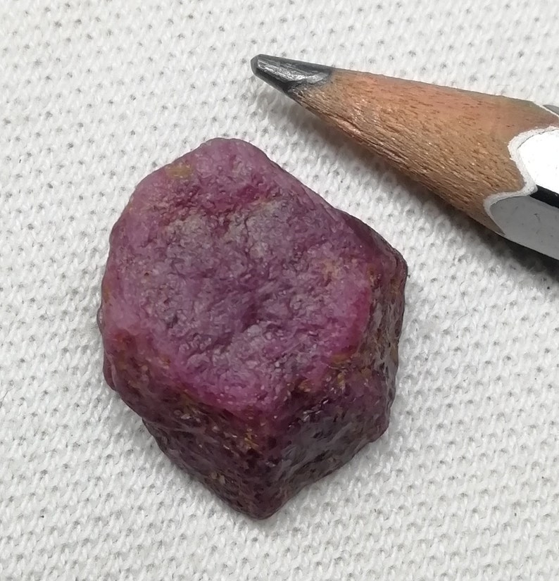 Op de afbeelding: Een diep roze, ruw geslepen robijn edelsteen. De robijn is ongeveer zo groot als een gum.