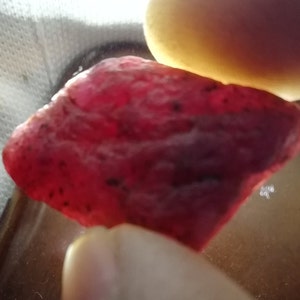 Peut inclure: Une grosse pierre pr&eacute;cieuse rouge brute avec une teinte rouge fonc&eacute;. La pierre pr&eacute;cieuse a une finition naturelle non polie.