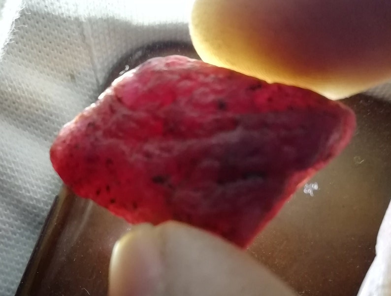 Peut inclure: Une grosse pierre pr&eacute;cieuse rouge brute avec une teinte rouge fonc&eacute;. La pierre pr&eacute;cieuse a une finition naturelle non polie.