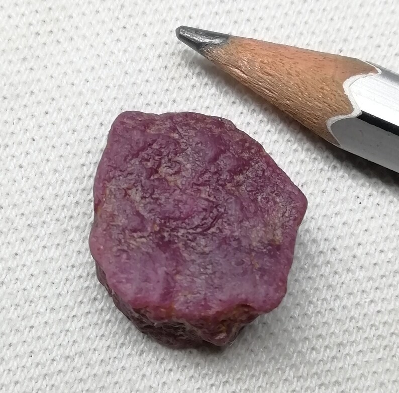 Op de afbeelding: Een ruwe, roze robijn edelsteen met een natuurlijke, onregelmatige vorm. De robijn is ongeveer zo groot als een gum.