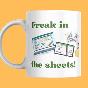 May include: White ceramic mug with the text "Freak in the sheets!" in green. The mug features illustrations of spreadsheets on a laptop and tablet, with charts and graphs. The mug has a curved handle.