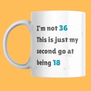 May include: White ceramic mug with a curved handle. The mug features the text "I'm not 36, This is just my second go at being 18" in a mix of grey and teal blue lettering. The mug is set against a yellow-orange background.
