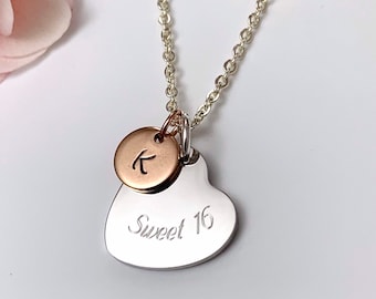 May include: Silver necklace with a heart charm engraved with "Sweet 16" and a smaller round charm with the letter "K" in rose gold.
