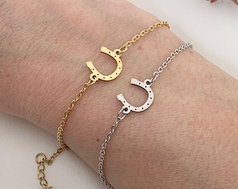 Puede incluir: Dos pulseras con un dije de herradura, una de oro y otra de plata. Las pulseras están en la muñeca. Los dijes de herradura están detallados con pequeños puntos.