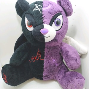 May include: A plush bear with a split design, featuring black fur on the left side and purple fur on the right. The black side has a red flame embroidery and a white sigil on the forehead. The purple side has a crescent moon and white wings.
