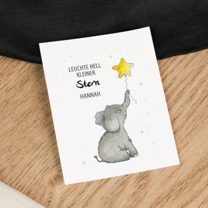 Op de afbeelding: Een grijze olifant die een gele sterballon vasthoudt met de tekst "Leuchte hell kleiner Stern Hannah" op een witte achtergrond.