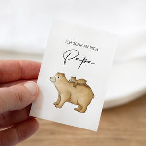 Può includere: Un biglietto bianco con un orso marrone e due cuccioli. Il testo sul biglietto recita "Ich denk an dich Papa".