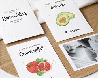 May include: Four white cards with black text and illustrations of a heart, an avocado, a pomegranate, and a photo of a baby. The cards are numbered 16 and 18. The text on the cards reads "Heute haben wir deinen Herzschlag zum ersten mal gehört", "Du bist so groß wie eine Avocado", "Du bist so groß wie ein Granatapfel", and "16. Woche" and "18. Woche".