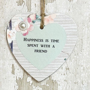 May include: A light green heart-shaped wooden sign with a white and pink floral design. The sign has a white pearl embellishment and the text "Happiness is time spent with a friend".