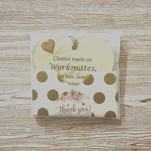 Puede incluir: Placa de madera en forma de coraz&oacute;n con el texto "Chance made us Workmates" y un peque&ntilde;o coraz&oacute;n de madera. Se empaqueta con una tarjeta de lunares blancos y dorados que dice "thank you!" con un dise&ntilde;o floral.