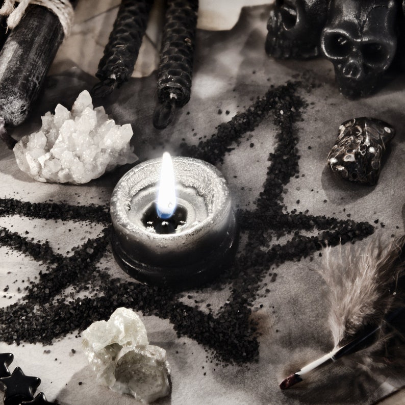 May include: A black candle with a white flame sits in the center of a pentagram drawn in black sand on a white surface. There are crystals, feathers, and other objects surrounding the candle.
