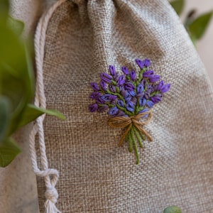 Peut inclure: Un petit sac en toile de jute beige avec un motif de fleurs de lavande cousu à la main. Le sac est fait de tissu naturel et a un aspect rustique et simple.