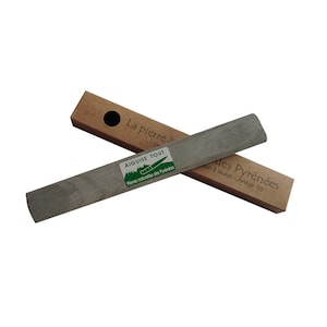 May include: A grey sharpening stone with the text "AIGUISE TOUT" and "Pierres naturelles des Pyrénées" on a green and white label. The stone is displayed with its brown cardboard packaging, which has the text "La pierre à" and "des Pyrénées".