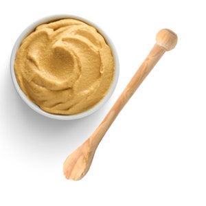 May include: A white bowl filled with yellow mustard and a wooden spoon.