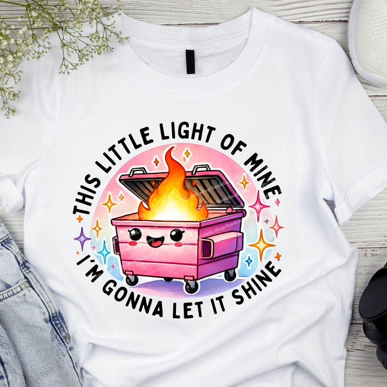 May include: White t-shirt with a pink trash can with a smiling face and flames coming out of it. The text around the trash can says "This little light of mine I'm gonna let it shine."