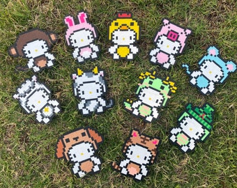 Può includere: Dodici diversi design di personaggi in pixel art con un personaggio Hello Kitty in vari costumi. I personaggi sono realizzati in feltro e sono alti circa 5 cm. I personaggi includono una scimmia, un coniglio, un pollo, un maiale, una mucca, una rana, un gatto, un cane, una tigre e una renna.