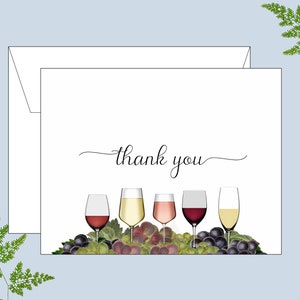May include: A white thank you card with a handwritten thank you message and a row of five wine glasses with different colored wine. The glasses are sitting on a bed of green grapes.