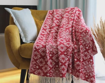 Peut inclure: Une couverture à motifs rouges et blancs avec des franges est drapée sur un fauteuil jaune moutarde. Un coussin bleu clair repose sur la chaise. La couverture présente un motif géométrique.