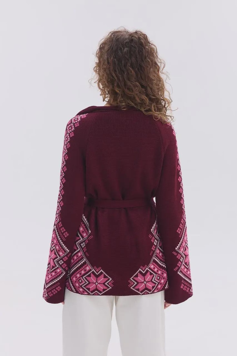 May include: A deep burgundy knit cardigan featuring long sleeves and a waist tie. The garment is decorated with a repeating geometric star pattern in shades of light pink and white along the sleeves and the lower back hemline.