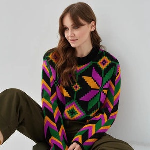 Puede incluir: Un su&eacute;ter negro con un patr&oacute;n geom&eacute;trico colorido en tonos de verde, morado, amarillo y naranja. El su&eacute;ter tiene mangas largas y cuello redondo.
