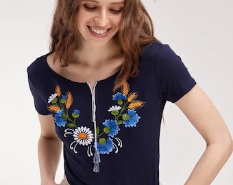 May include: A navy blue short-sleeved t-shirt with a white embroidered floral design on the front. The design features blue and yellow flowers, green leaves, and wheat stalks.