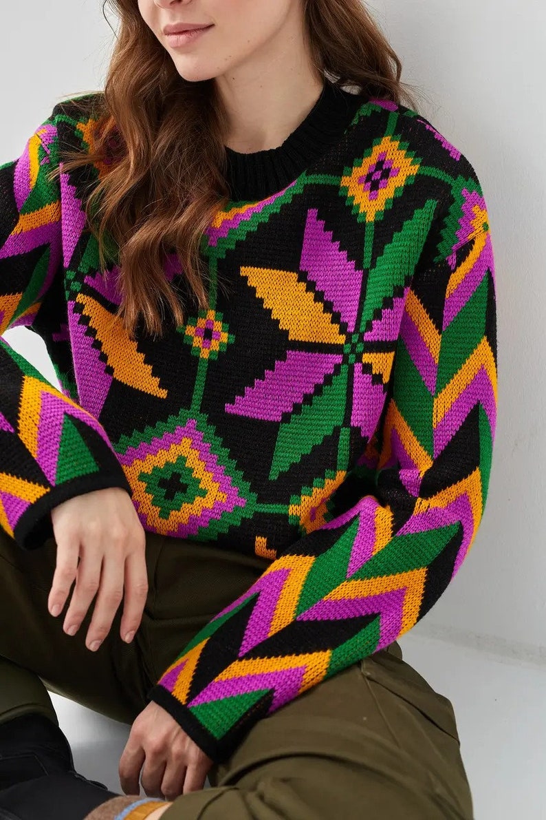 Puede incluir: Un su&eacute;ter negro con un patr&oacute;n geom&eacute;trico colorido en tonos de verde, morado y amarillo. El su&eacute;ter tiene cuello redondo y mangas largas.